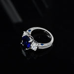 Bague saphir diamant avec un saphir bleu ovale et un anneau en argent serti de zircones.