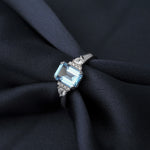 Bague topaze bleue avec un anneau en argent sterling 925 glissée sur un tissu foncé.