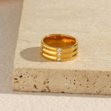 Bague trois anneaux dorés en acier posée sur une table.