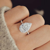Main portant une bague de fiançailles avec une pierre en forme de poire et un anneau pavé.