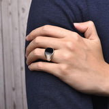 Chevalière homme bague argentée avec une pierre noire ovale portée au doigt d'un homme.