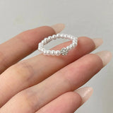 Elastique bague pour femme en perles blanches avec un strass métallique.