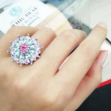 Grosse bague argent femme originale avec une grosse fleur en pierres précieuses, portée sur l'annulaire d'une femme.