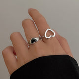 Main de femme portant une bague cœur ajouré de couleur argent et une bague coeur avec pierre noire.