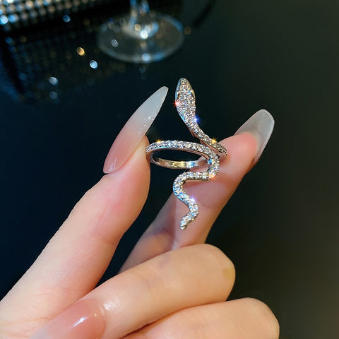 Bague serpent de couleur argentée, entièrement sertie de strass, tenue entre deux doigts.